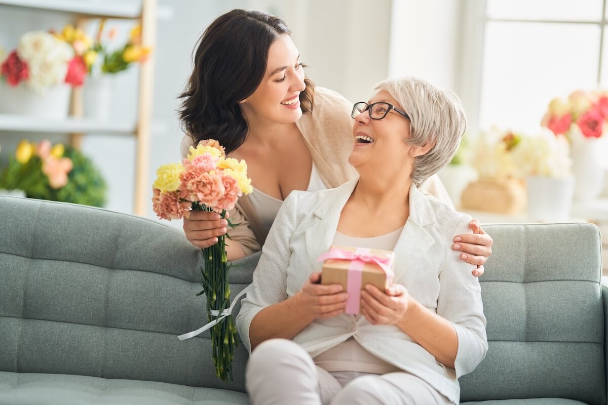 Smiling adult daughter surprising her mom with flowers