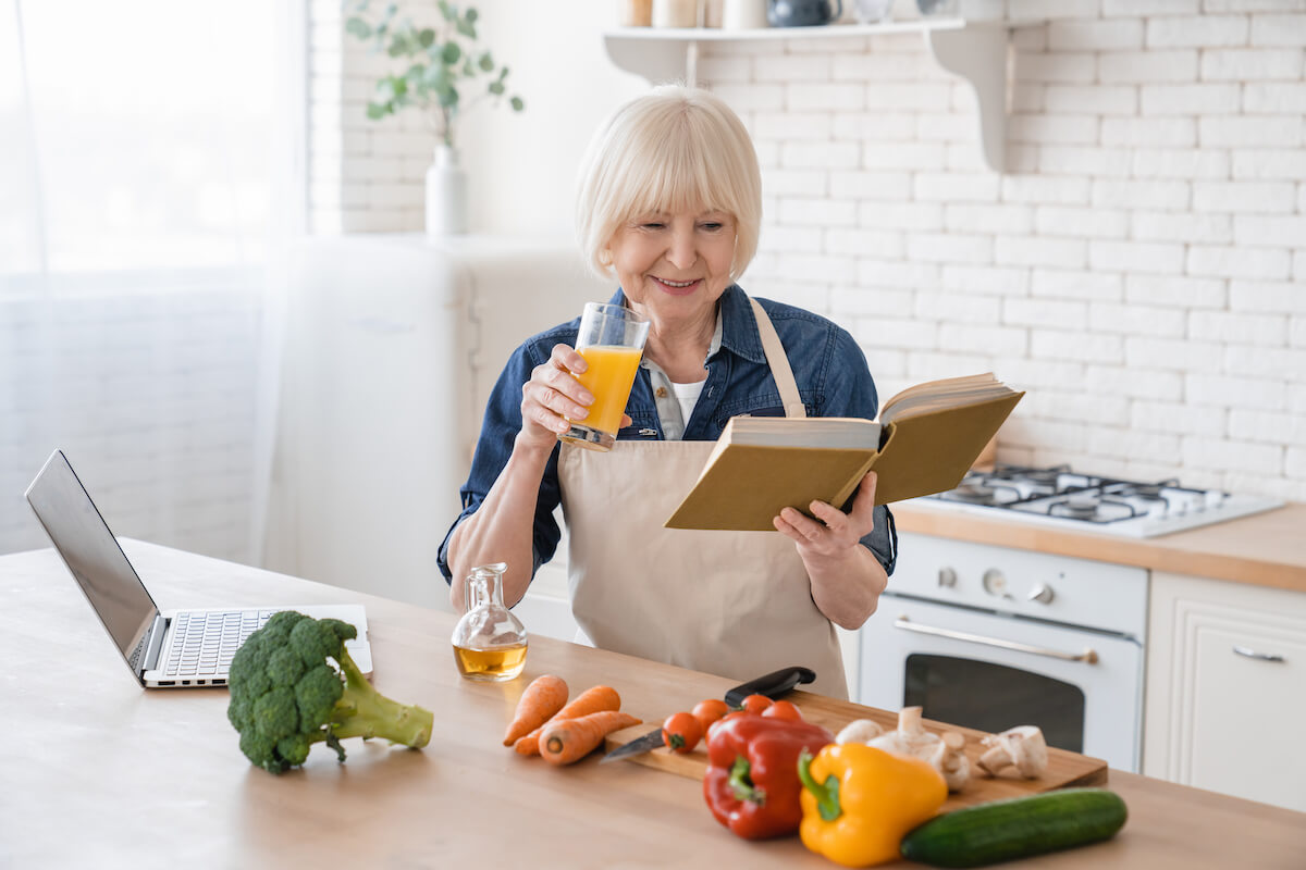 Older woman reading a book for healthy eating in her kitchen